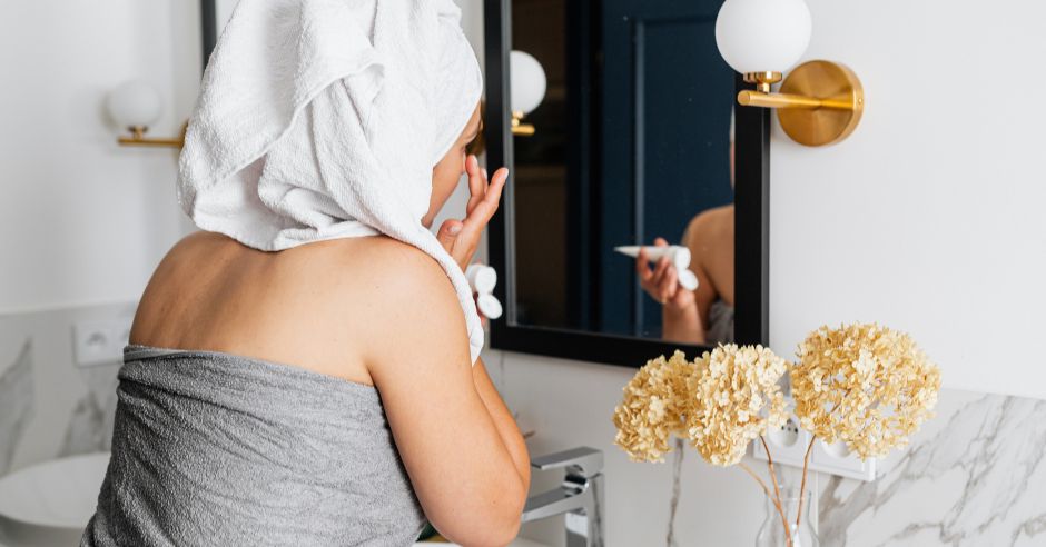 Жінка наносить крем на обличчя перед дзеркалом